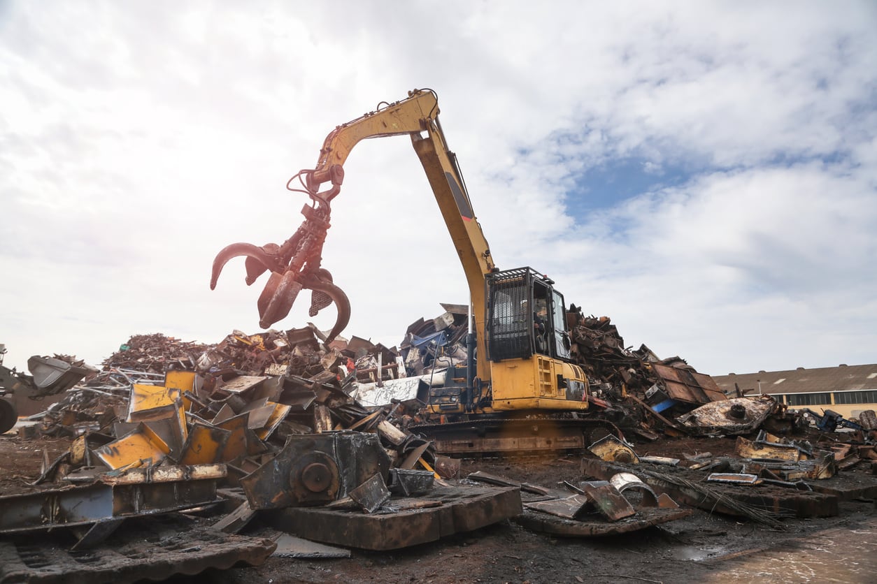 An image of a yellow waste machine with a robotic claw on the top of a mound of crap metal.