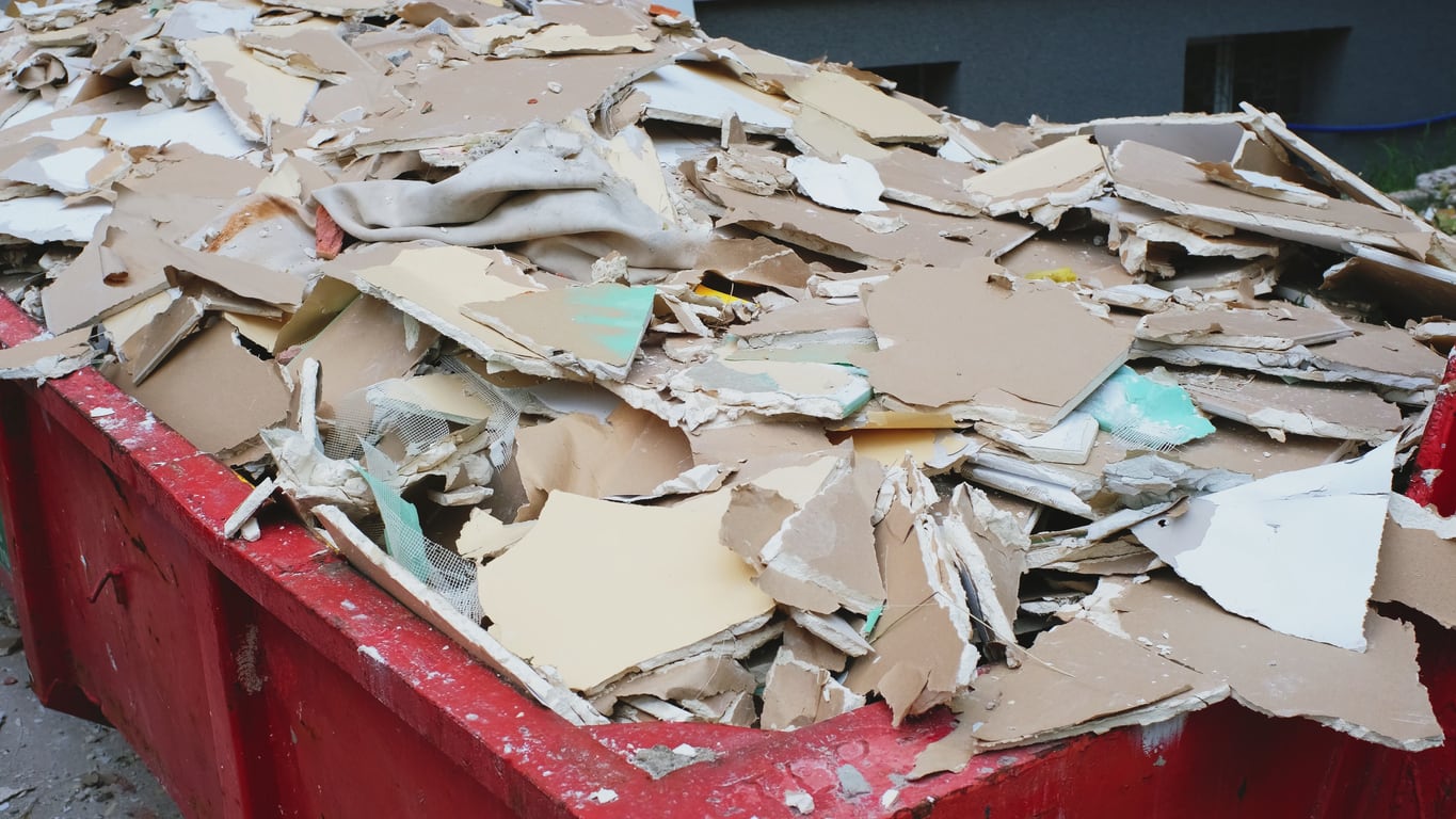 Image or various plasterboard off cuts of different shapes in sizes, filling a large skip.